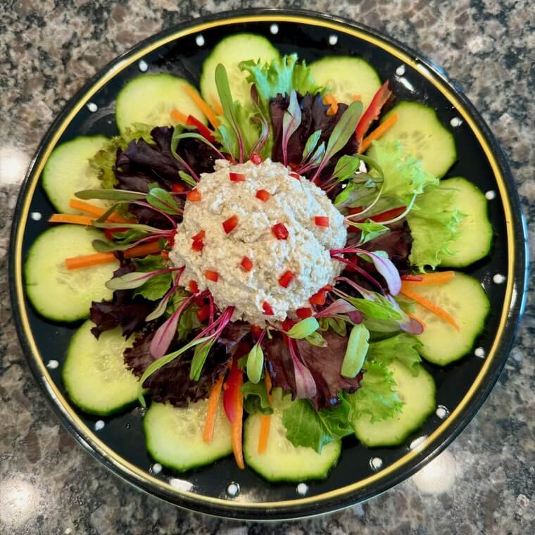 Raw vegan salad with a cauliflower center, microgreens, and cucumber slices on a black polka-dot plate
